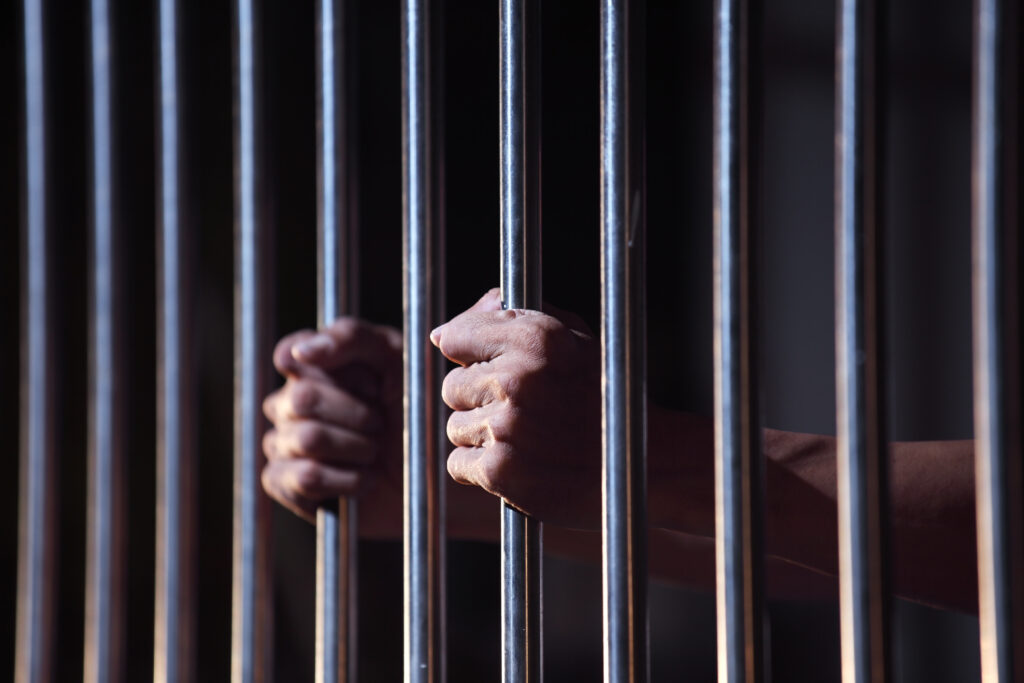 Prisoners hands holding bars of a jail