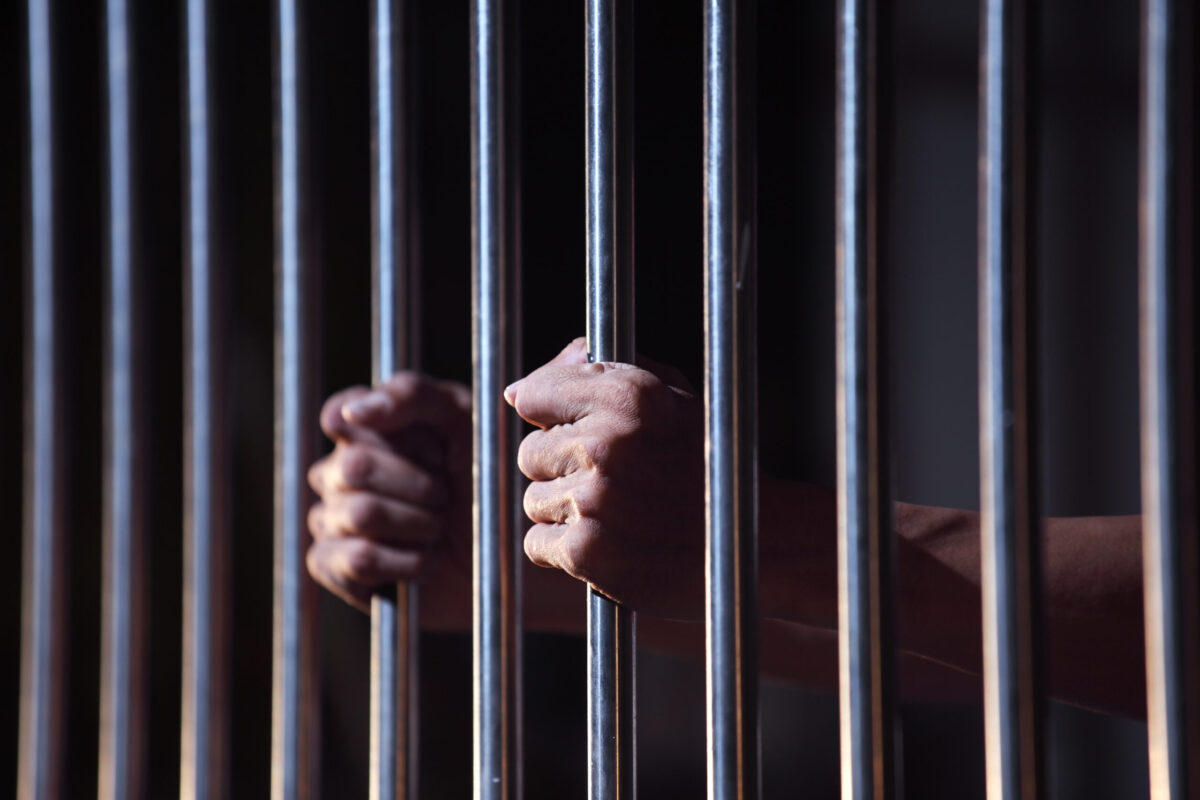 Prisoners hands holding bars of a jail